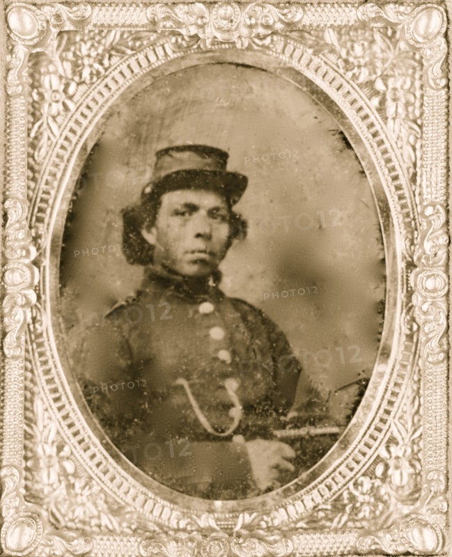 Black soldier seated with pistol in hand, watch chain in pocket