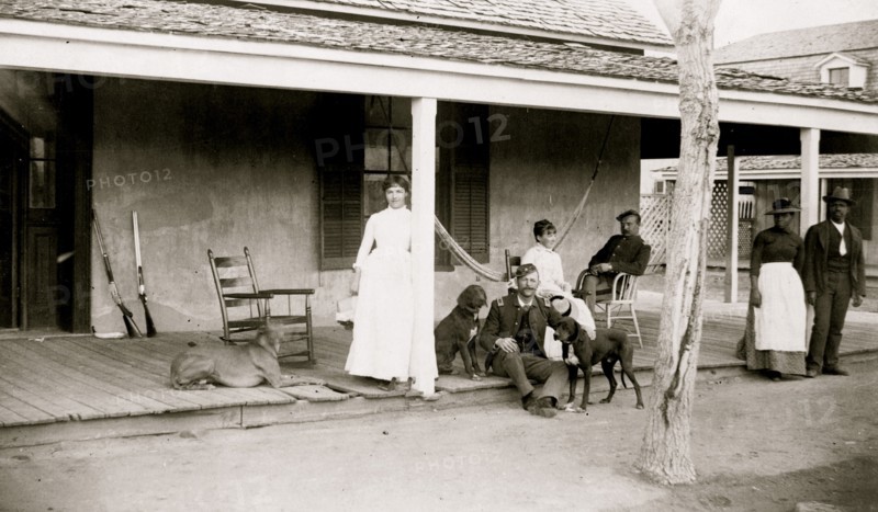 Two soldiers and two women on porch, with Afro-American woman and man to right, Fort Verde, Arizona
