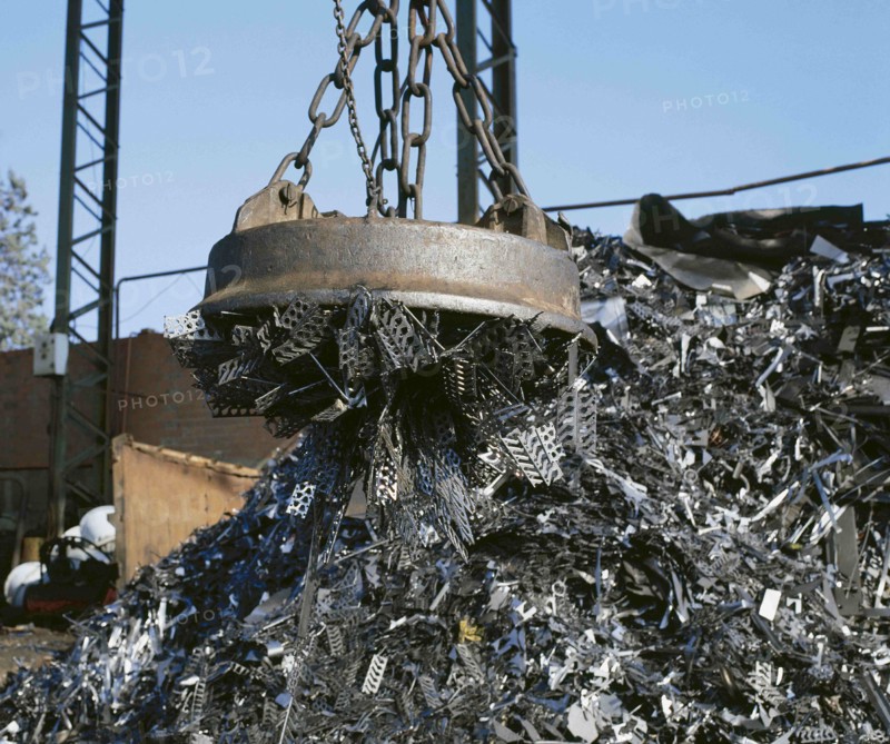 Electromagnet on crane lifting metal at scrap yard.