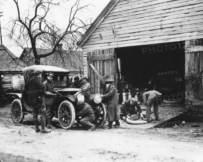 An early touring car stops at a gas station for repairs. No location, early 1900s.