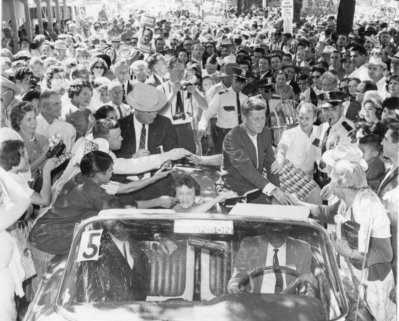 Senator John F. Kennedy (right) and Senator Lyndon B. Johnson (left with hat), along with Senator Kennedy's mother Rose Kennedy (center, seated in car), are greeted by supporters as they leave Burnett Park enroute to Dallas, Texas. The two were in the State campaigning for the presidential and vice presidential post of the US on the Democratic ticket. Fort Worth, Texas, 1960.
