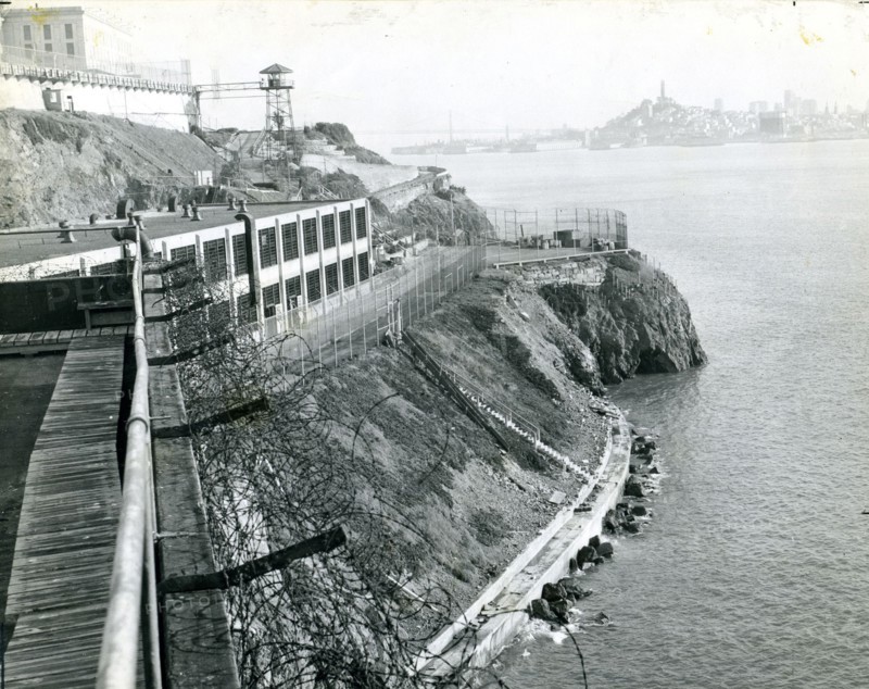 Alcatraz Prison, San Francisco, CA, circa 1940 - A view of the island taken from the industrial area with a guard tower, main cellhouse and San Francisco skyline in the background.