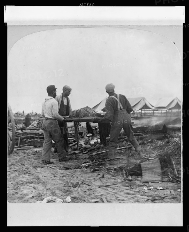 Galveston, Texas, 1900 - African-American men carrying a body on a stretcher, surrounded by wreckage of the hurricane and flood. Stereograph.