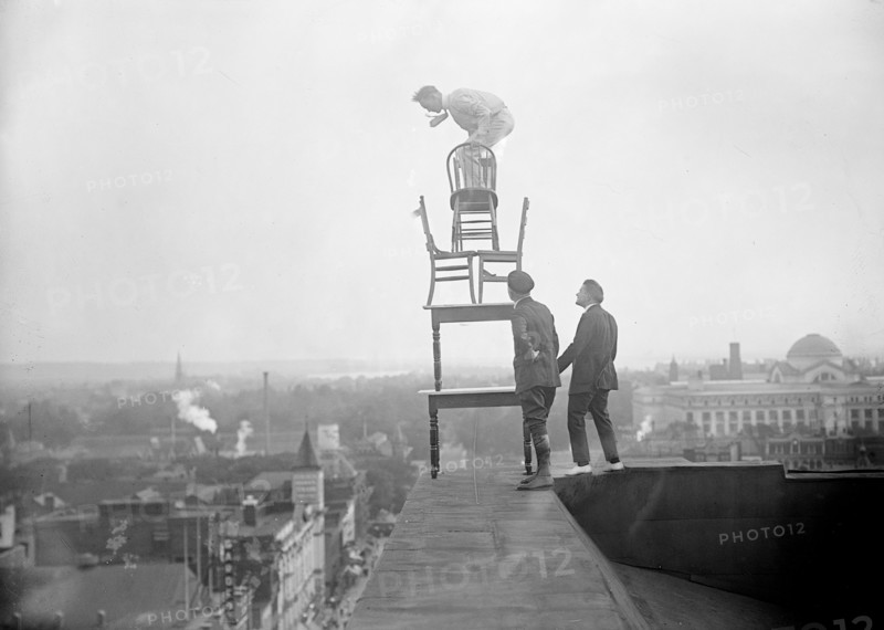 J. Reynolds Acrobat, performing acrobatic and balancing acts on top of building above 9th Street NW in Washington D.C. circa 1917.