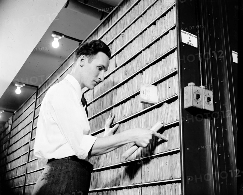 Patent Office employee pointing to copies of first patent granted after 1836 when patent laws were rewritten circa 1940.