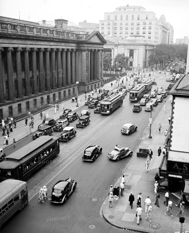 Pedestrians, cars and street cars near Treasury Department on 15th Street in Washington D.C. circa 1936.
