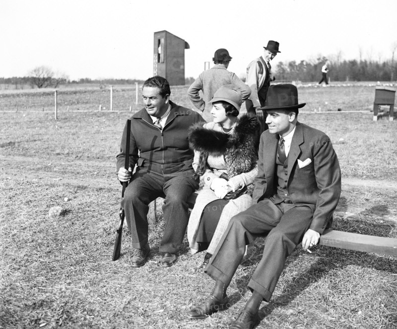 Man holding rifle or shotgun, with a man and woman possibly at a shooting range circa 1936.