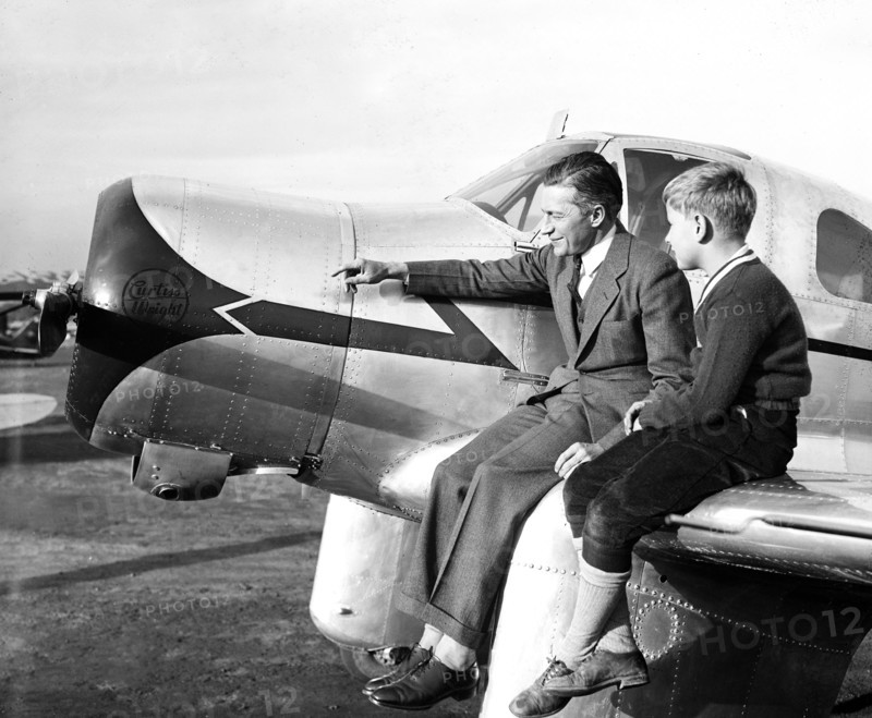 Man and his son sitting on the wing of a Curtiss airplane circa 1936.