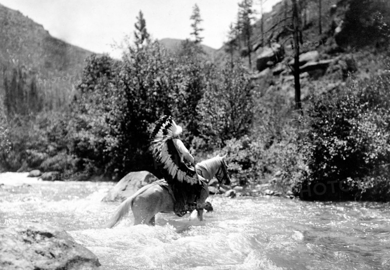 Edward S. Curtis Native American Indians - Bullchief, wearing warbonnet, crossing shallow rapids on horseback circa 1905.