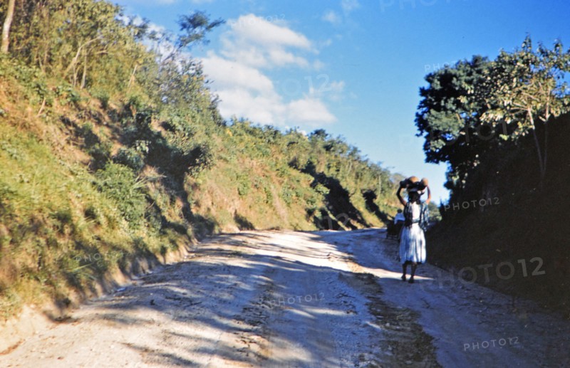 1962 Guatemala - Woman carrying food or package on her head down road to a village in Guatemala.
