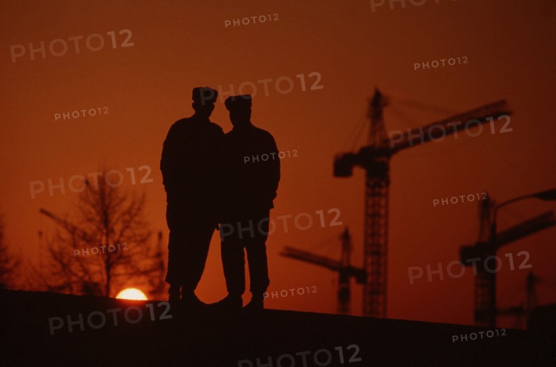 East German policemen stand atop a section of the Berlin Wall at sunset..