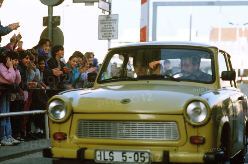 West German children applaud as an East German couple drive through Checkpoint Charlie and take advantage of relaxed travel restrictions to visit West Germany..