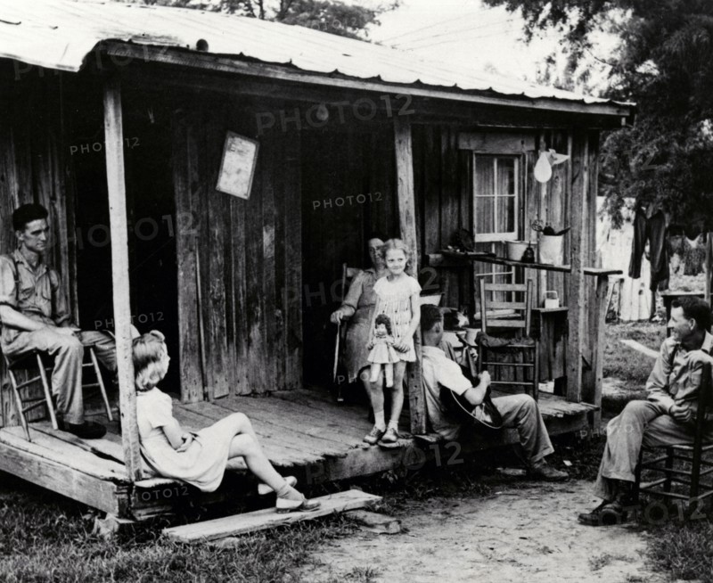 A rural family sits on an unscreened porch in the early evening