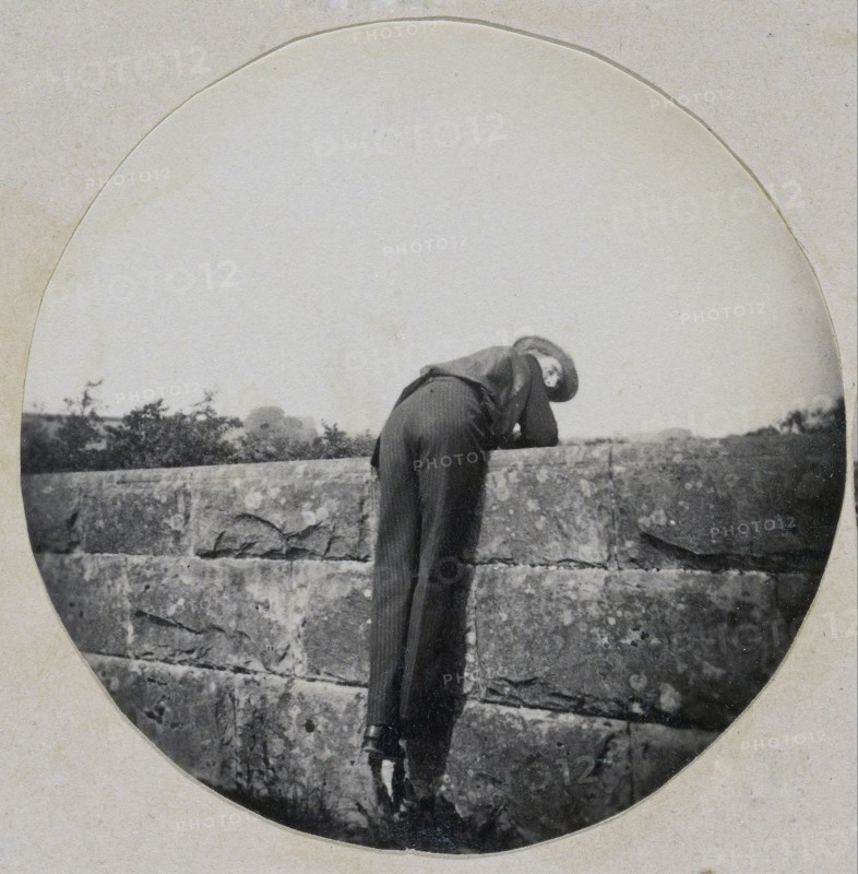 Man in Hat Bent Over a Stone Wall