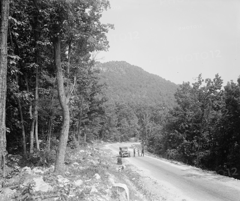Men standing outside a car on a rural road ca.  between 1910 and 1926