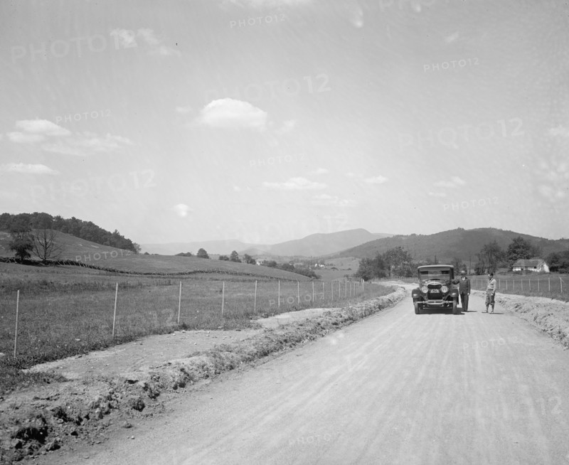 Two men standing outside an automobile on a rural road ca.  between 1910 and 1926
