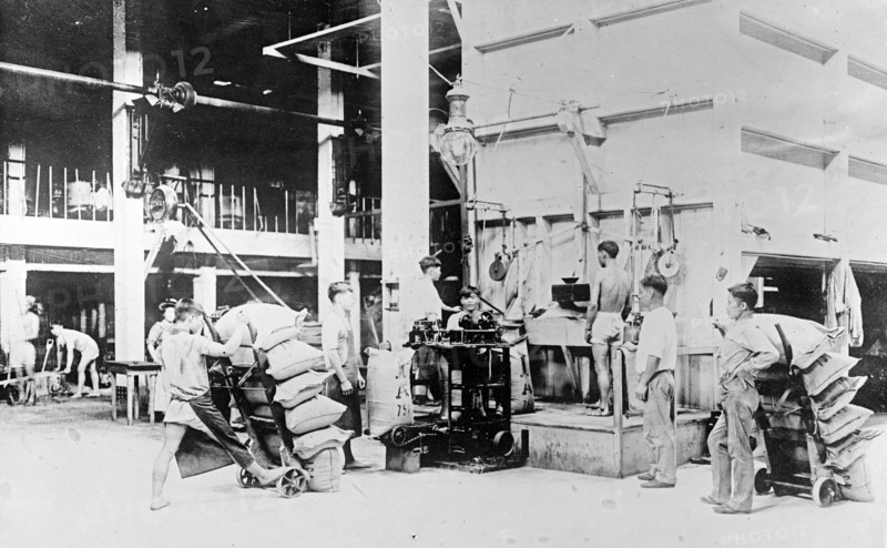 Filling, weighing and sewing sacks of raw sugar at Plantation mill, Hawaiian Islands ca. 1910 to 1920