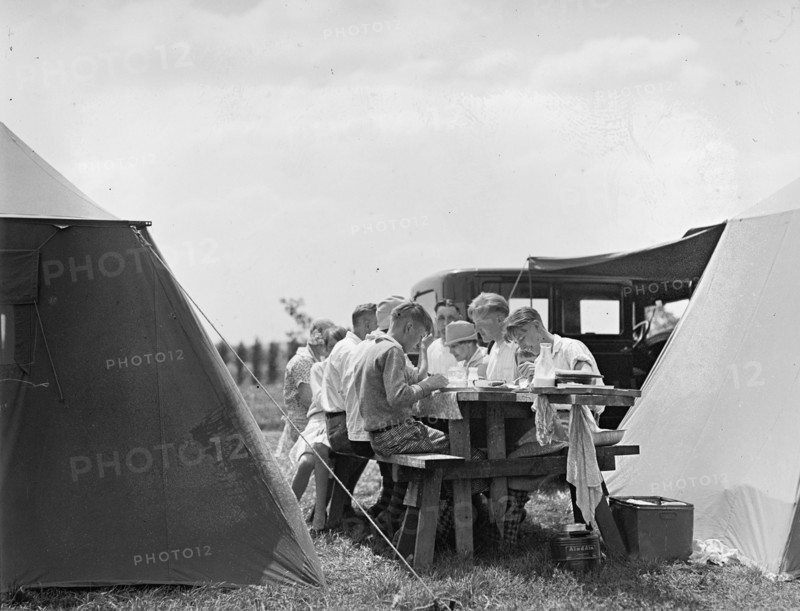 A family eating at a picnic table while camping in the early 20th century ca. between 1909 and 1923