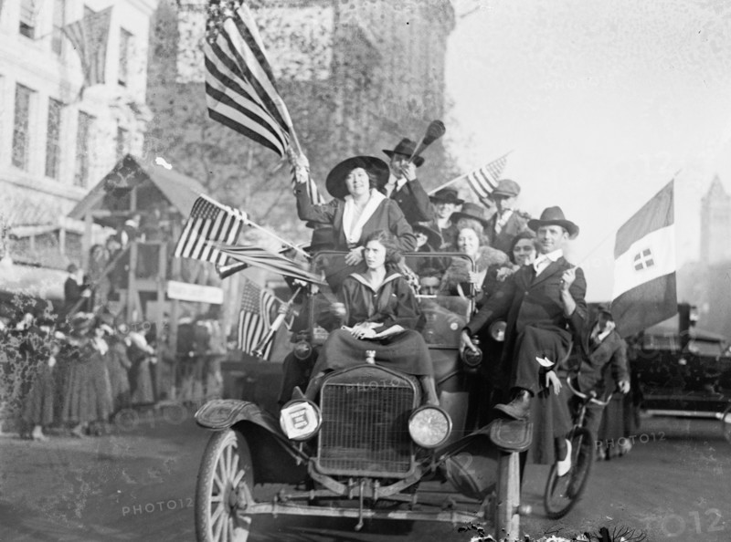 Men and women in an overcrowded car waving American flags during a peace demonstration ca.  1918