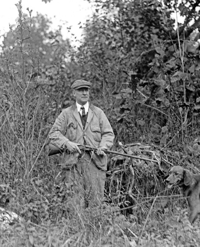 Miles Poindexter holding a shotgun (or rifle) with his hunting dog  ca.  between 1918 and 1920
