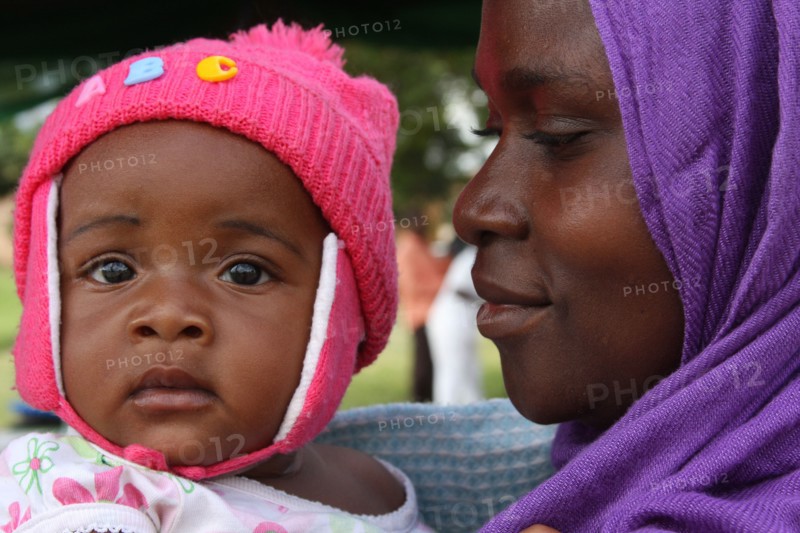 A woman in a purple head scarf looks lovingly at her daughter Angel (Tanzania) ca. 4 March 2014