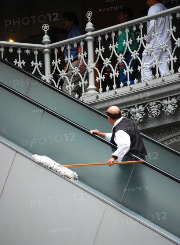 Worker at the Crescent Court Hotel in Dallas, TX; man cleaning with dust mop, riding an escalator