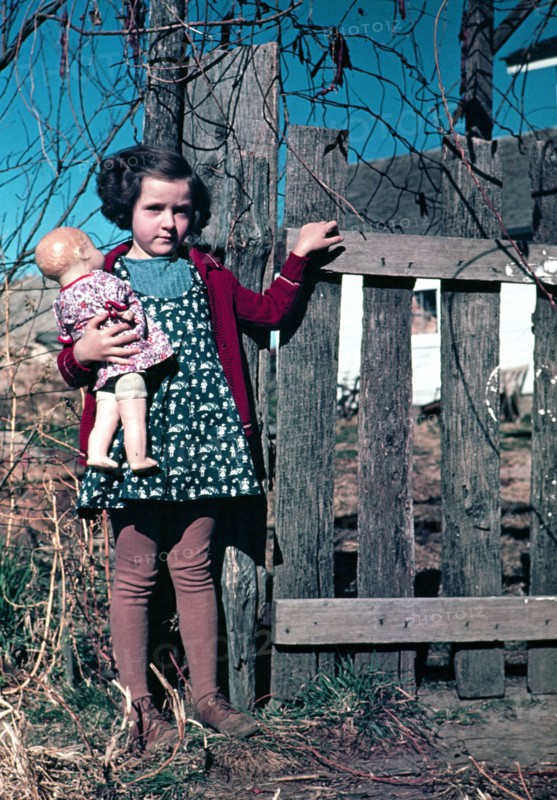 Girl with doll standing by fence