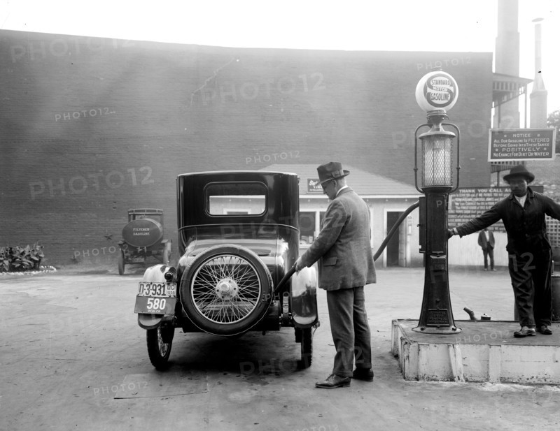 Man pumping gas into his automobile in early 1900s