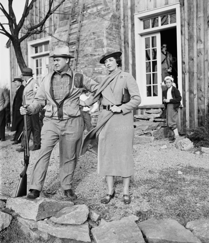 Well dressed woman with man holding rifle or shotgun