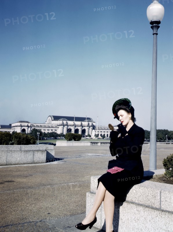 Woman putting on her lipstick in a park with Union Station behind her