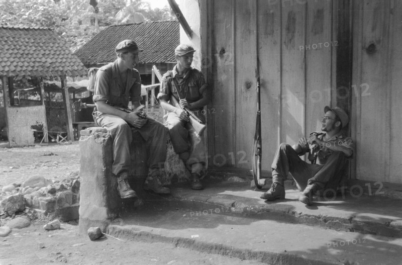 Operation Schoonschip. Three soldiers are resting in front of a building in a kampong; Date March 29, 1949; Location Indonesia, Dutch East Indies