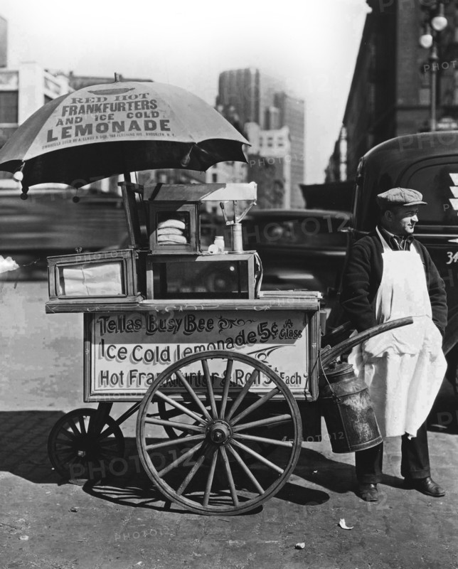 1930s New York City - Hot Dog Stand, West St. and North Moore. Vendor stands next to his Tellas Busy Bee cart, advertising 'Red Hot Frankfurters and Ice Cold Lemonade' ca. 1936