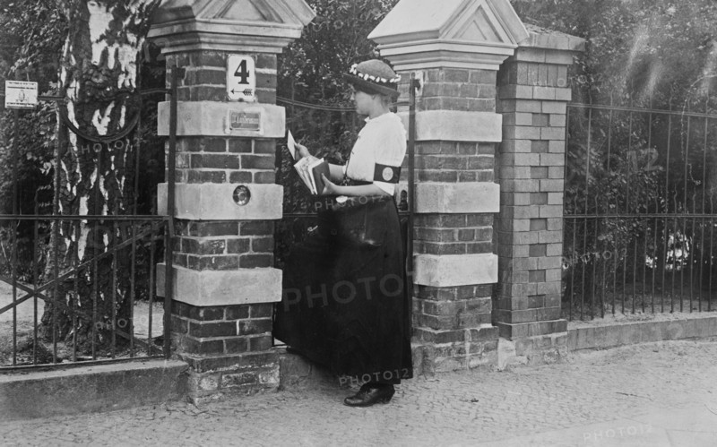 Woman mail carrier at a gate of a house, in Berlin, Germany during World War I ca. 1910-1915