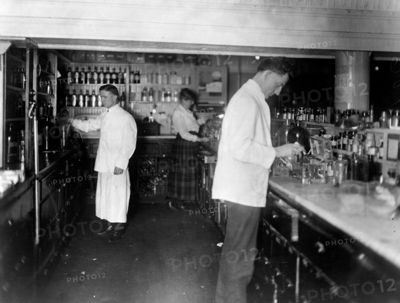 Pharmacists at People's Drug Store, 7th and E Streets, N.E., Washington, D.C., at counter preparing medications ca. 1909-1932