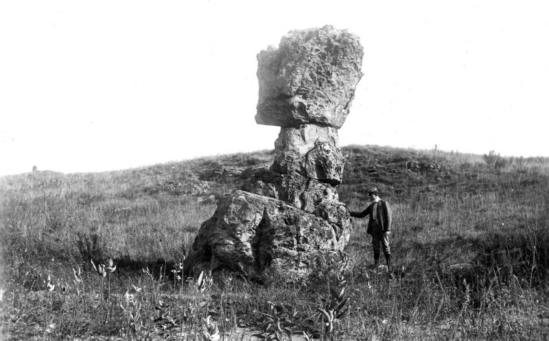 August 28th, 1901 photo of a gentleman with his hand on a leaning tower of St. Peter Sandstone as a result of post-glacial weathering near Footville, Wisconsin. (Leaning tower of rock).
