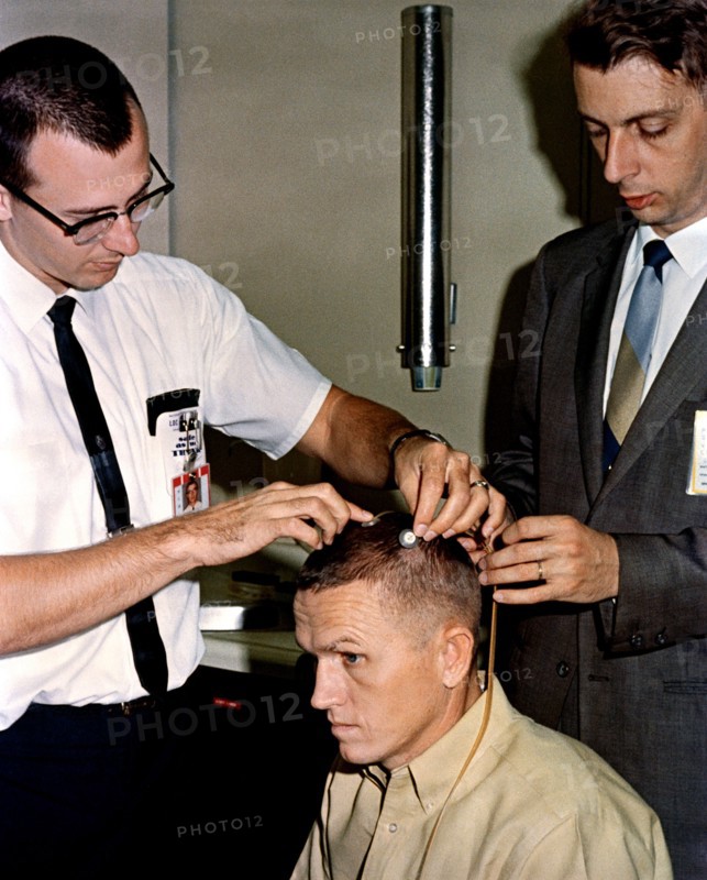 (2 Dec. 1965) Astronaut Frank Borman, Gemini-7 command pilot, sits attentively as two scalp electrodes are attached to his head.