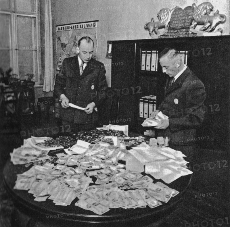 Preparation for shipment to Berlin of transport of gold coins and foreign currency stolen from Jews in Litzmannstadt Ghetto. Hans Biebow, first from the right ca. 1941-1943