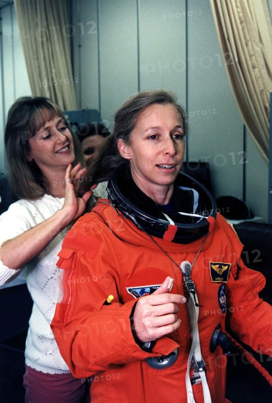 STS-81 Mission Specialist Marsha S. Ivins gets a helping hand from a suit technician as she prepares to don the helmet of her launch/entry suit in the suitup room of the Operations and Checkout (O&C) Building ca. 1997