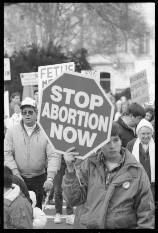Young person holding a sign that has "Stop Abortion Now" written on it at a pro-life march, Washington, DC, 1/22/1990.