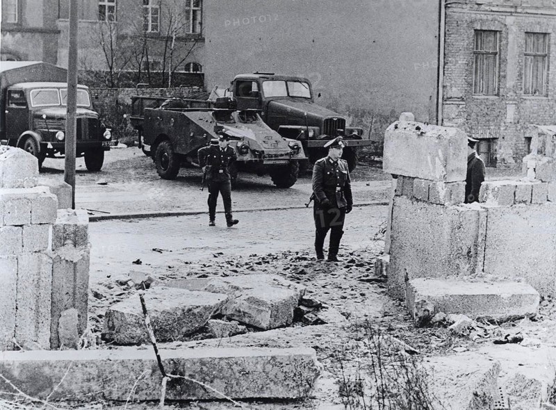 The refugees rammed the wall with a heavy truck and then fled on foot into the French Sector of West Berlin when their truck stalled in the rubble. The East German guards fired several shots at them but missed. In the background are Communist military vehicles posted after the incident to prevent further escapes.