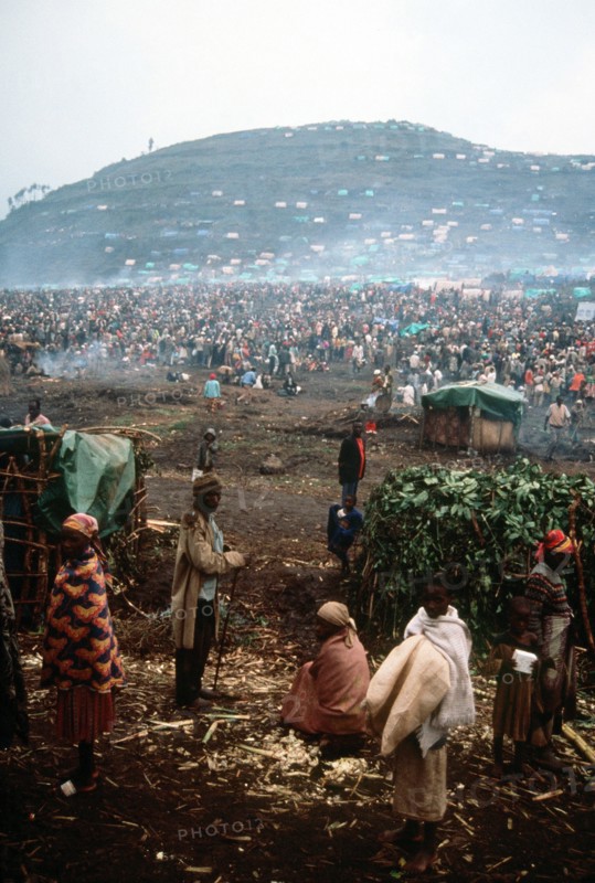 1994 - A group of refugees with the refugee camp in the background.
