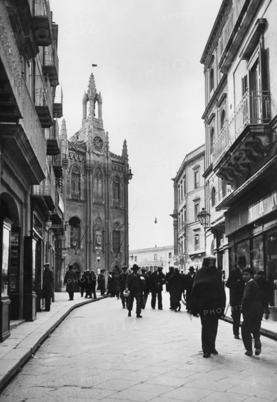 europe, italie, sicile, agrigento, personnes dans la rue avec le bâtiment de la chambre de commerce en arrière-plan, 1934
