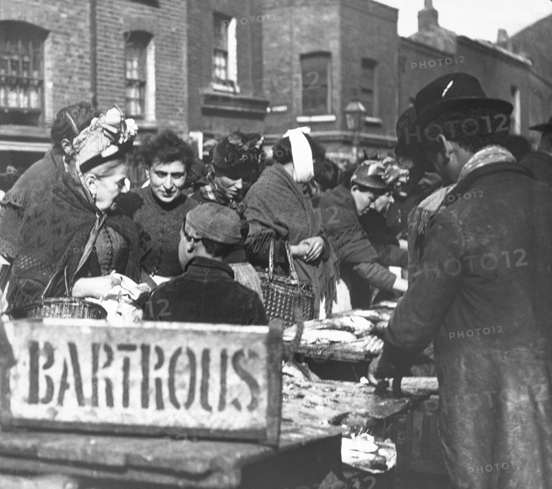 A fishmonger stall in the market with lots of people buying fish.