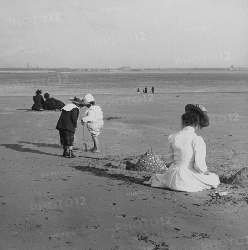 Beach scene with children playing and adults sitting in the sun.