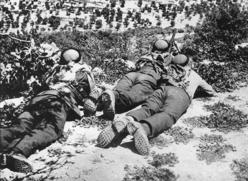 Three Arab soldiers lying on the ground overlooking a valley in Palestine.  They are guarding against attacks from Jewish soldiers.