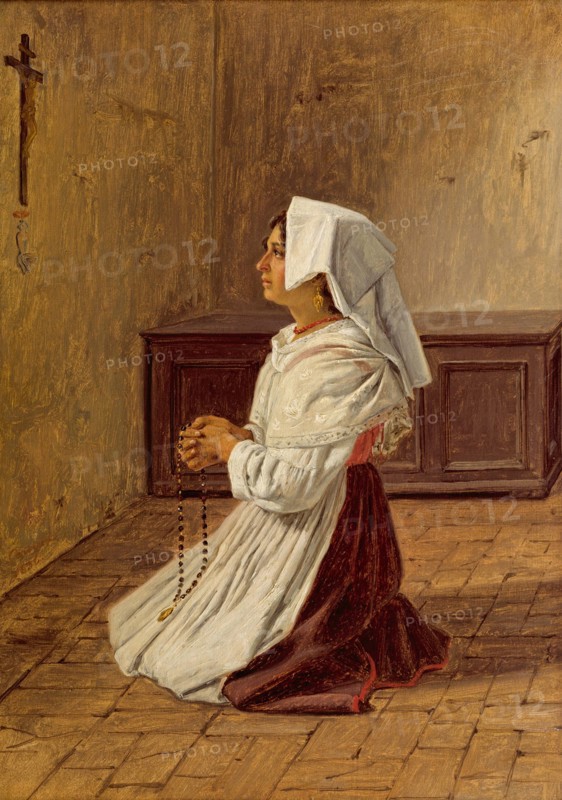 woman prays on her knees in front of a cross on the wall
