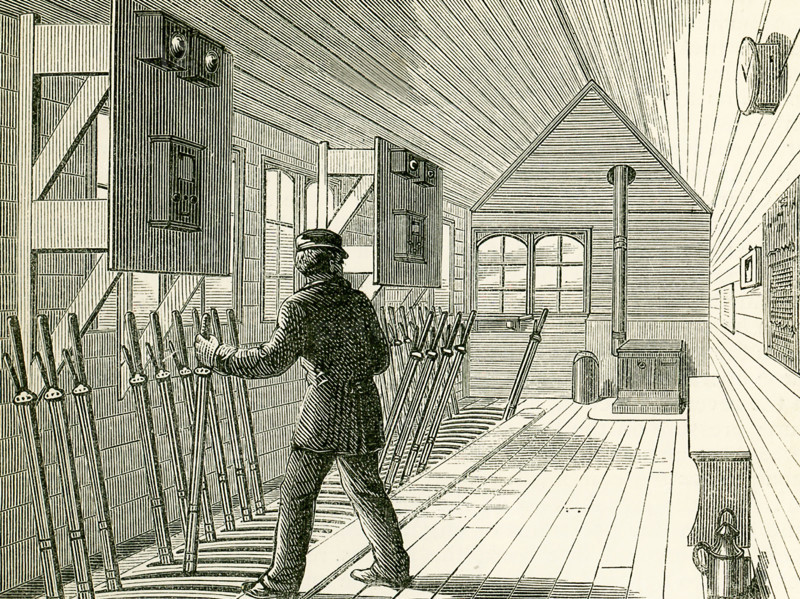 This illustration dates to the 1870s and shows the signal box on the North London Railway. The interior of a signal-box near an important junction or station is shown here, and we see here the numerous levers for working the points and the signals, each of these having a connection, by rods or wires, with the corresponding point or signal-post. The electric telegraph is now an important agent in railway signalling, and in a signal-box we may see the bells and instruments which inform the pointsman whether a certain section of the line is ""blocked"" or ""clear."" The signals now generally used on British railways are made by the semaphore, which is simply a post from which an arm can be made to project. When the driver of the train sees the arm projecting from the left-hand side of the post, it is an intimation to him that he must stop his train; when the arm is dropped half-way, so as to project 45¬8 from the post, it is meant that he must proceed cautiously; when the arm is down the ...