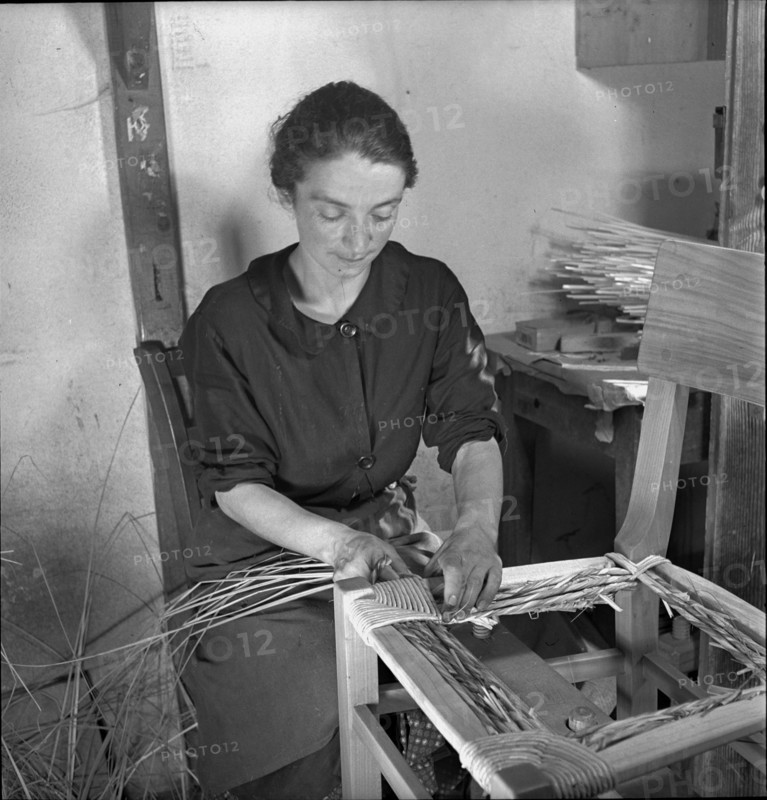 Woman braiding straw around a chair, 1940.