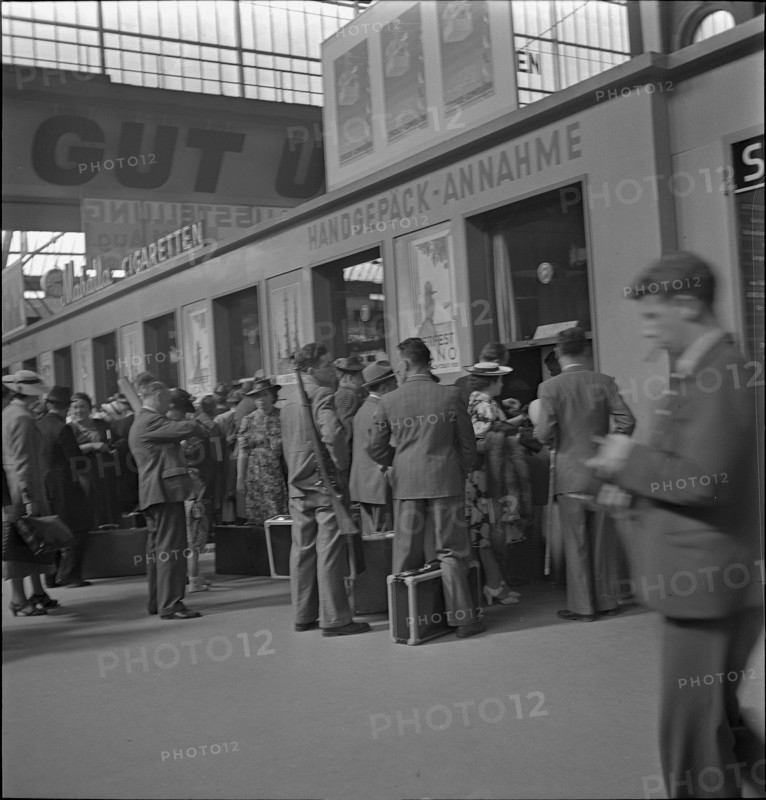 People queue at in-counter of luggage office ; 1939