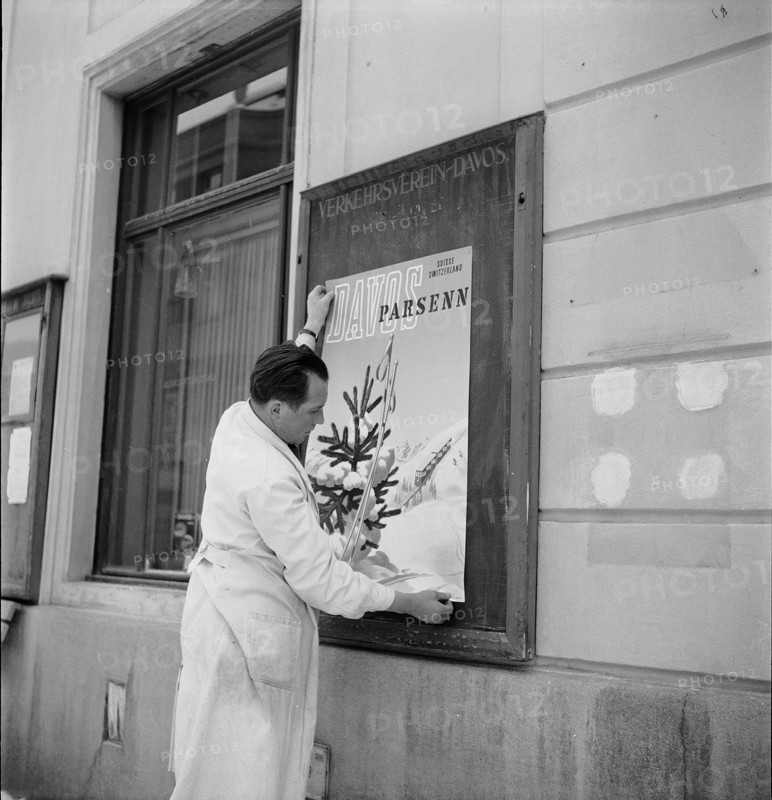 Davos: Man hangs up a poster of the tourist association; 1949
